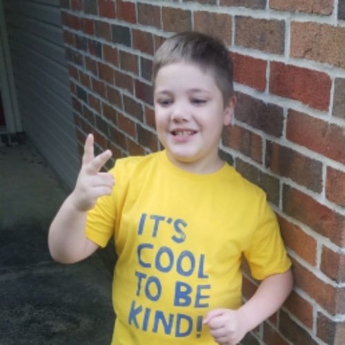 A young boy proudly wears a shirt that reads "It's cool to be kind," promoting a positive message of kindness.