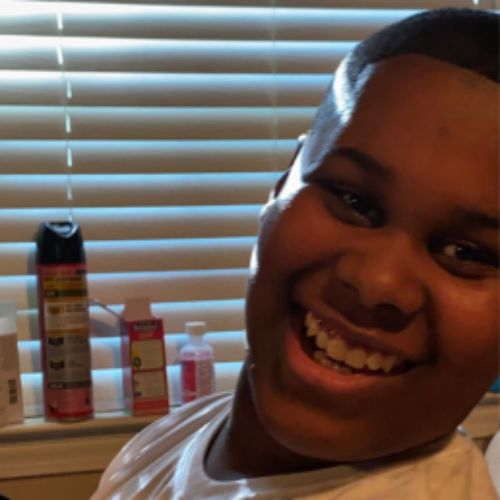 A young boy smiles brightly while seated in front of a mirror, reflecting joy and innocence in his expression.