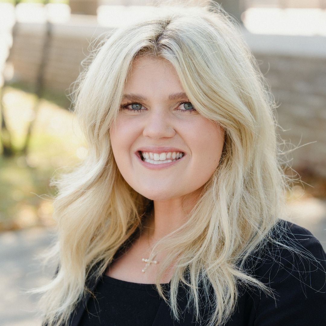 A woman with long blonde hair wearing a black blazer, exuding professionalism and confidence in her appearance.