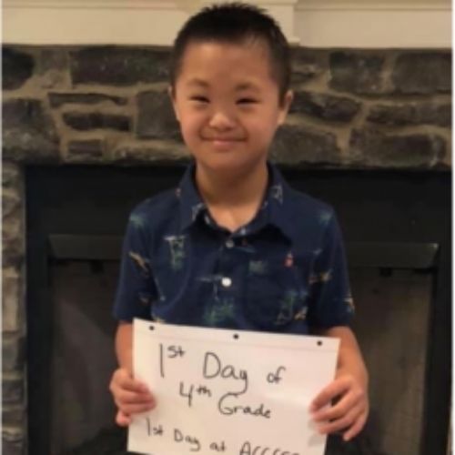 A young boy proudly displays a sign reading "1st Day of 4th Grade," showcasing his joy and excitement.