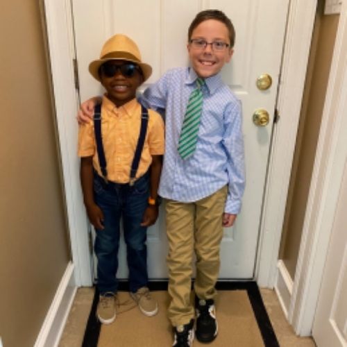 Two boys in ties and hats pose confidently in front of a door, showcasing their stylish attire and cheerful demeanor.