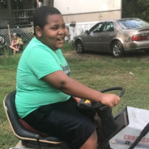 A young boy sits on a lawn mower, enjoying a fun and adventurous ride in a grassy area.