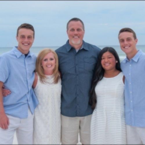 A family smiles together for a photo on the beach, with waves and sand in the background.