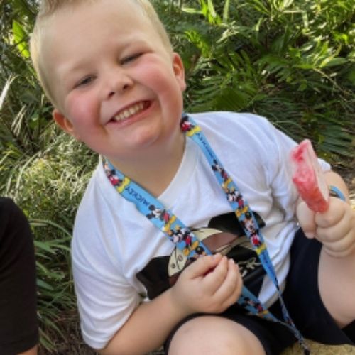 A young boy sitting on the ground, smiling joyfully at the camera, capturing a moment of happiness.