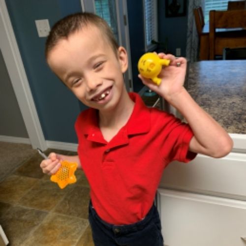 A young boy grips a yellow toy in one hand, showcasing a moment of playful curiosity.