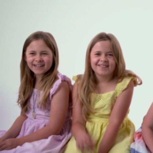 In a studio setting, two young girls sit together, sharing smiles and laughter as they interact with one another.