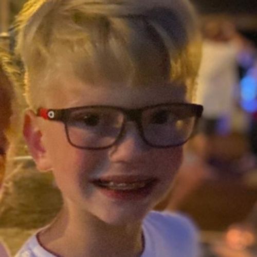 A young boy with glasses smiling brightly at the camera, showcasing his cheerful expressions and friendly demeanor.