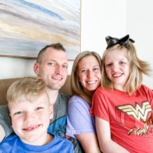 A family of four sits together on a couch, enjoying quality time with their young children in a cozy living room setting.