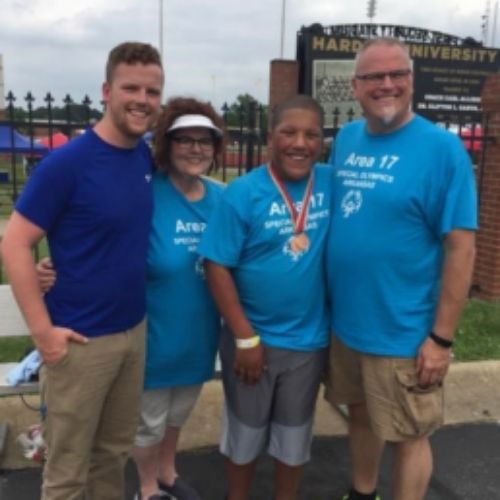 Four individuals wearing blue shirts are standing closely together, smiling and engaging with one another.