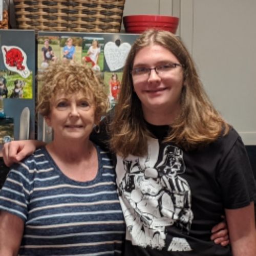 A woman and a young man stand together in the kitchen, posing for a photo with their arms around each other, showcasing connection.