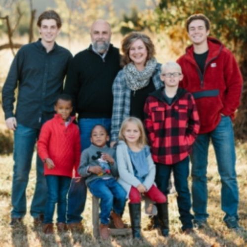 A cheerful family poses for a photograph in a vibrant field, enjoying a sunny day together amidst nature.