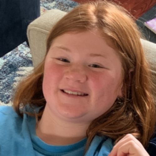 A young girl with vibrant red hair is seated comfortably on a couch, exuding a sense of relaxation and contentment.