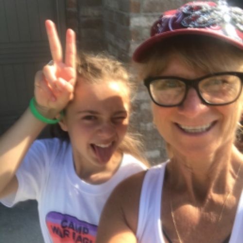 A woman and a young girl smile brightly while making the peace sign with their fingers, radiating joy and positivity.