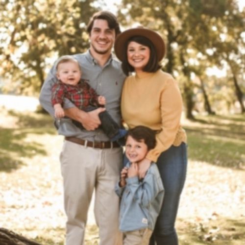 A family smiles together for a photo amidst colorful autumn leaves in a picturesque fall setting.