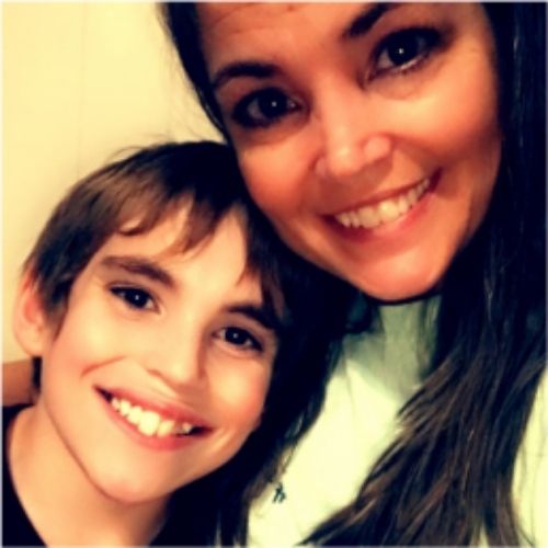 A woman and a boy smile brightly at the camera, capturing a joyful moment together.