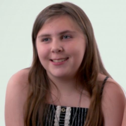 A young girl smile brightly while looking directly at the camera, radiating joy.