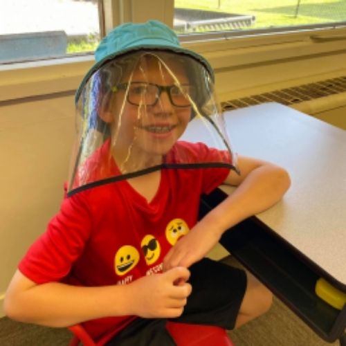 A young boy wearing a clear plastic face shield, showcasing safety and protection in a bright environment.