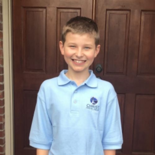 A young boy wearing a blue polo shirt stands confidently in front of a closed door.