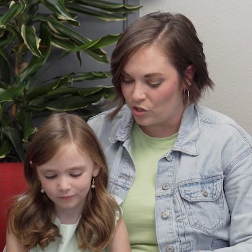 A woman and a young girl sit together on a couch, sharing a moment of warmth and companionship.