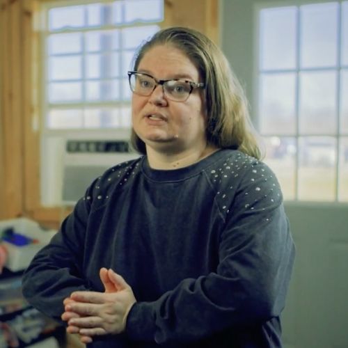 A woman wearing glasses and a black shirt is engaged in conversation, expressing her thoughts clearly.