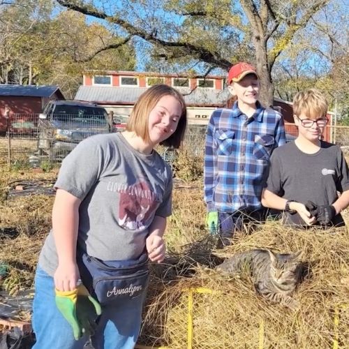 Three young individuals gather around a large pile of hay, engaged in conversation and enjoying the rural setting.