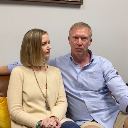 A man and woman are seated on a couch in a modern office environment, engaged in conversation.